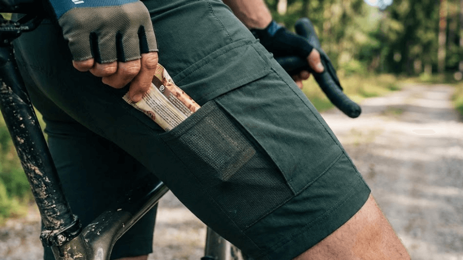 Close-up van de zak op het bovenbeen van een gravel kleding broek (Cargo Bib Short), waarin een telefoon of energiereep veilig is opgeborgen.