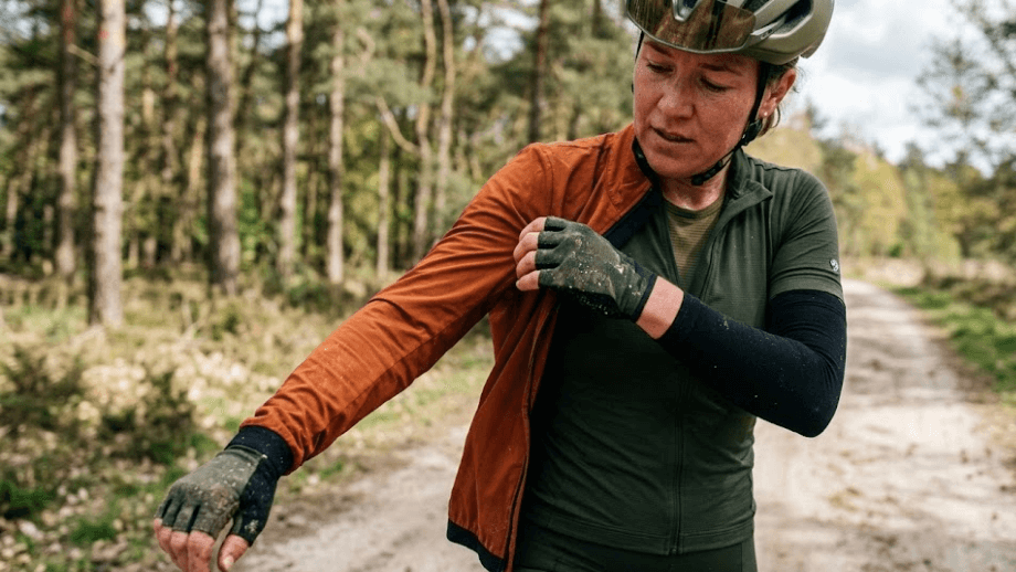 Een gravelbiker trekt tijdens een pauze zijn bodywarmer uit, een perfect voorbeeld van hoe een modulair laagjessysteem fietskleding werkt in wisselvallig weer.